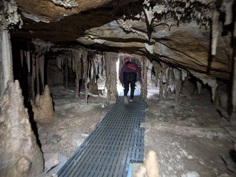 A grated path between cave formations, with one person farther along the walkway.