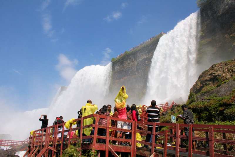 Visitors in yellow ponchos stand on red-painted timber walkways below the falls.