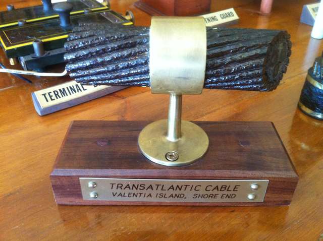 A short thick armoured cable sample on a brass-and-wood stand, labelled Transatlantic Cable, Valentia Island, Shore End.