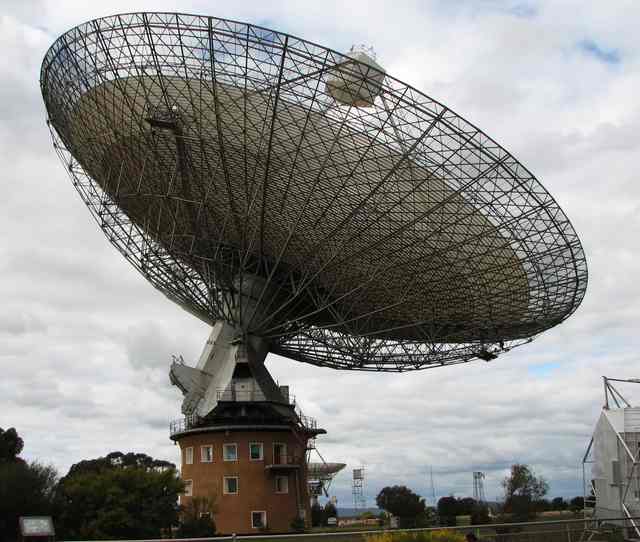 The broad radio dish and its framework sit above a tilting mount and round brick tower.