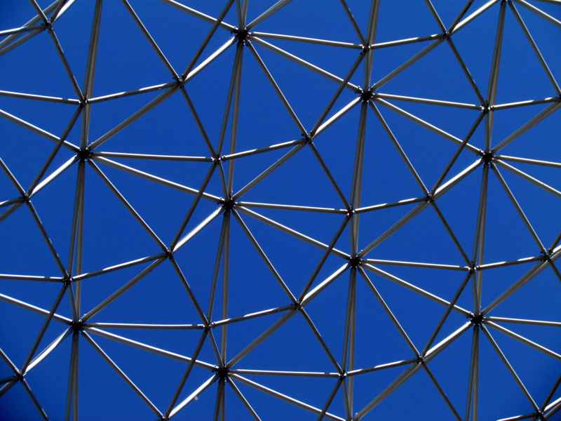 Intersecting metal tubes form overlapping triangles against a deep blue sky.