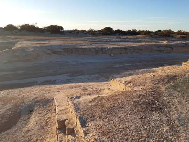 A broad shallow quarry with pale cut ledges and block outlines under a low sun.