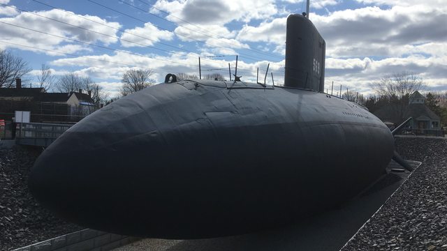 The rounded dark bow, long hull and sail of USS Albacore above its dry museum berth.