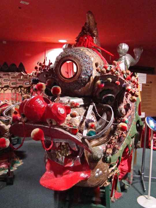 Loong’s elaborate head fills the view, with mirrors, coloured tufts, curled ornaments and a red tongue against the museum’s red interior.