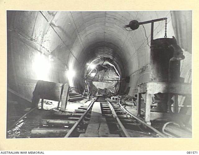 Rails and construction equipment fill an arched tunnel in a historic black-and-white photograph.