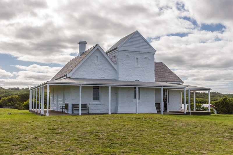 White-painted telegraph station with gabled roofs and a wraparound veranda beneath a cloudy sky.