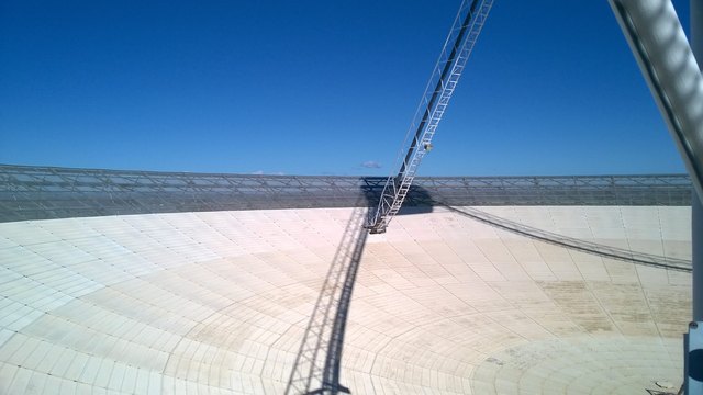 A view across the pale curved dish surface toward its metal outer rim and supporting struts.