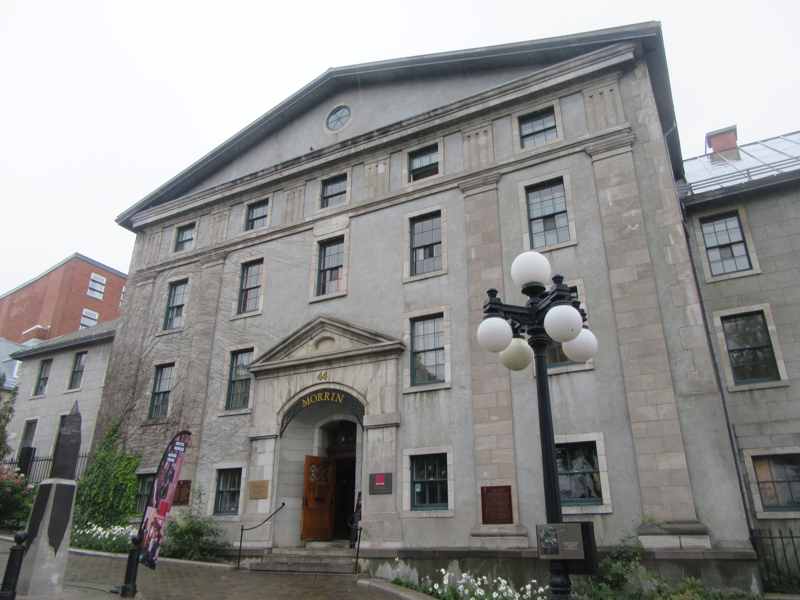 A symmetrical pale-stone building has a pedimented entrance marked Morrin and 44, with a globe streetlamp in front.