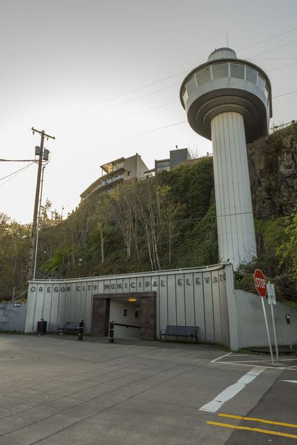 Concrete elevator shaft and rounded observation deck rising beside a bluff above the signed Oregon City Municipal Elevator tunnel entrance.