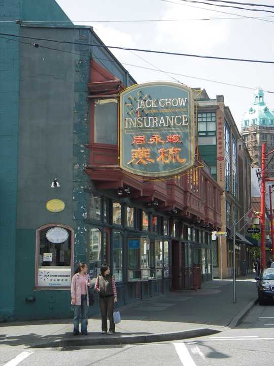 Daylight street view of a narrow two-storey building with projecting bays, a commercial sign and two pedestrians.