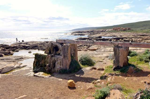 A timber channel crosses stone piers to the waterwheel beside a rocky bay.