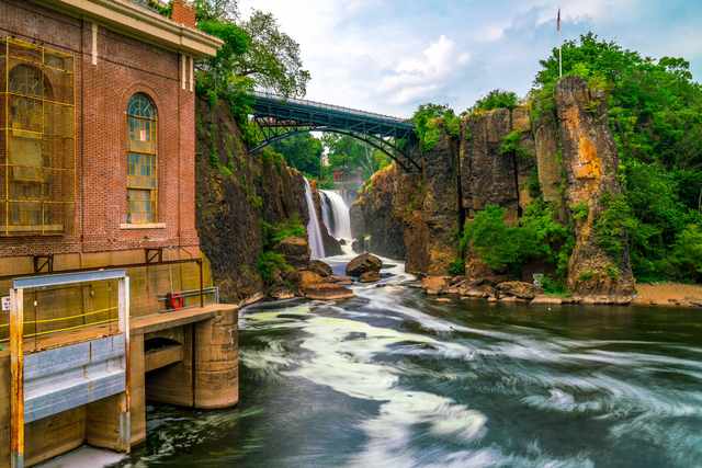 Tall arched windows on the powerhouse fill the left side of a closer view of the falls; a long exposure blurs the water below.