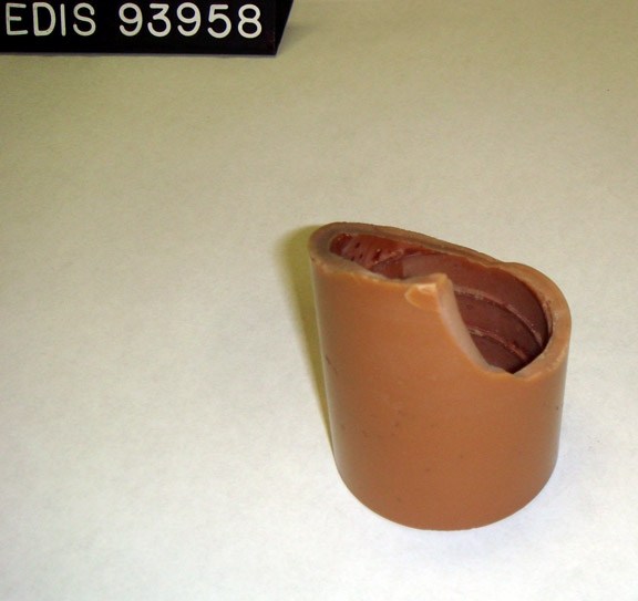 A brown wax cylinder with an uneven, partly missing upper rim beside a label reading EDIS 93958.