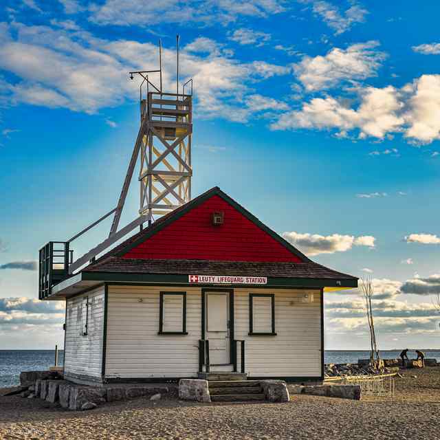 A closer view of the red-roofed station and white lookout tower, surrounded by rocks beside the lake.