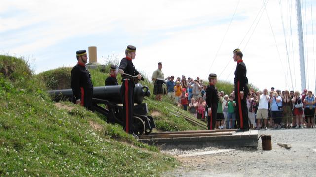 Costumed interpreters stand beside a cannon as visitors watch a public demonstration.