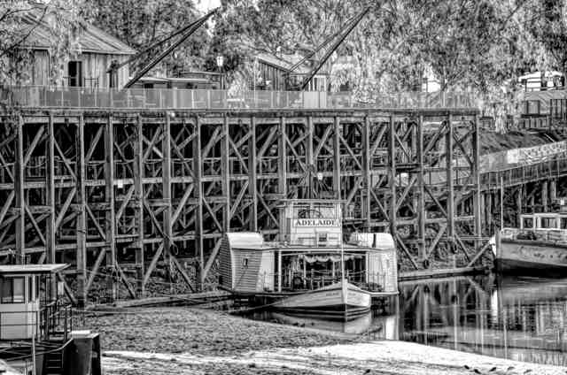 A paddle steamer named Adelaide beneath a tall timber wharf, with cranes and buildings on the upper deck.