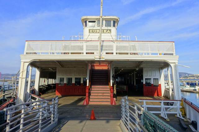 The end of a white ferryboat, with a central staircase, open lower deck and pilot house above.