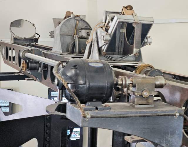 Circular mirrors, metal mounts and a geared shaft seen close up along the beam.