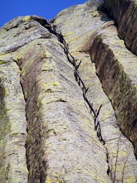 Wooden rungs and an outer rail rise through a narrow cleft between tall rock columns.