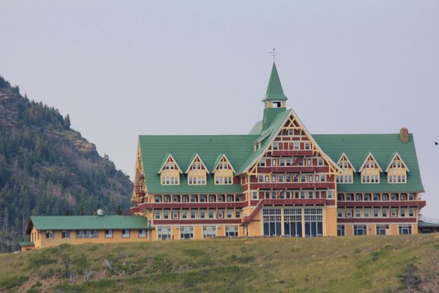A timber-faced hotel with a central tower, steep gables and long wings stands on a grassy hillside above the lake.