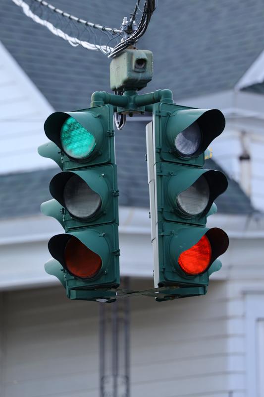 Two faces of a hanging traffic signal; the upper left lamp glows green and the lower right lamp glows red.