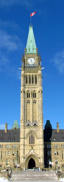 The Peace Tower rises above its stone entrance to a copper spire and Canadian flag, with small visitors at the steps.