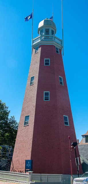 The red tapered Portland Observatory rises to a white viewing gallery with flagpoles; the photographer’s copyright credit remains at lower left.
