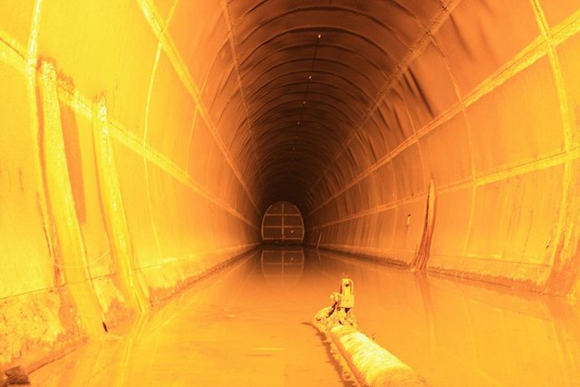 Orange lighting illuminates an arched, metal-lined tunnel and its reflective floor.