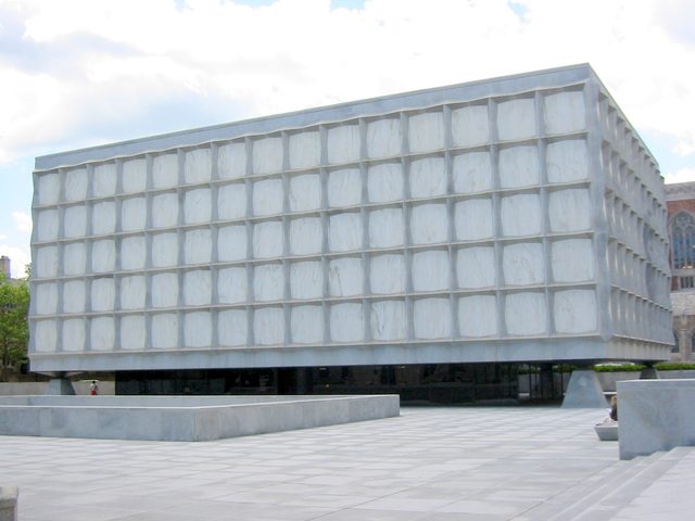 A rectangular library clad in pale stone panels stands above a recessed glass entrance level.