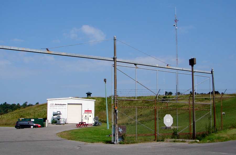 Low museum entrance building, grass-covered mound, antennas and a fenced gate at Carp.