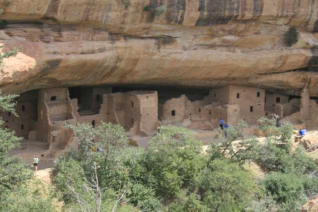A closer view of masonry rooms and openings beneath the sandstone overhang, with incidental visitors in 2006.