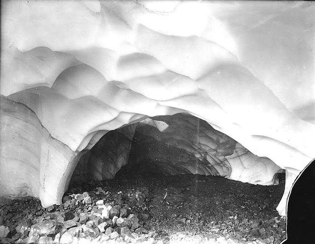 A broad sculpted ice ceiling curves over a rocky cave floor.