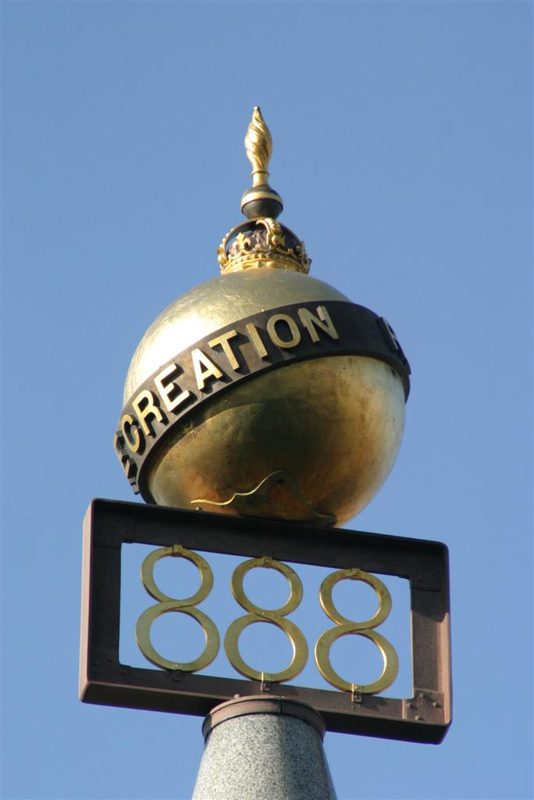 Three gold-coloured eights sit below a globe encircled by a dark band bearing the word Recreation, with a small crown and flame-shaped finial above.